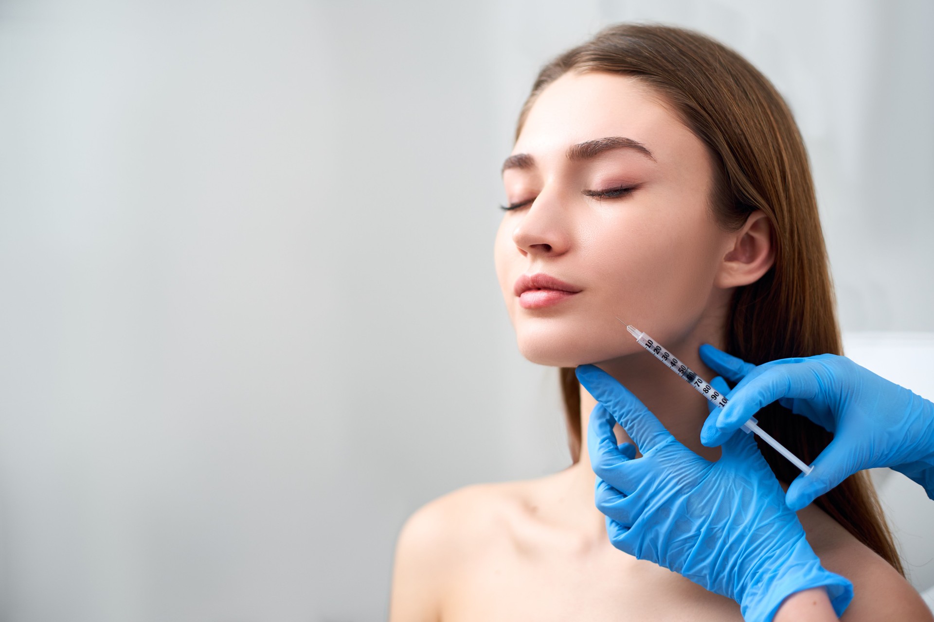 Smile lifting and lip augmentation. Dermatogist doctor hands doing beauty procedure to female face with syringe. Young woman's mouth countouring with filler injection. Marionette lines treatment